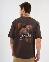 Person wearing a brown graphic t-shirt with a Jaguar design and text on the back. (DISCOVERY Men's Jaguar Graphic Tee - Truffle)
